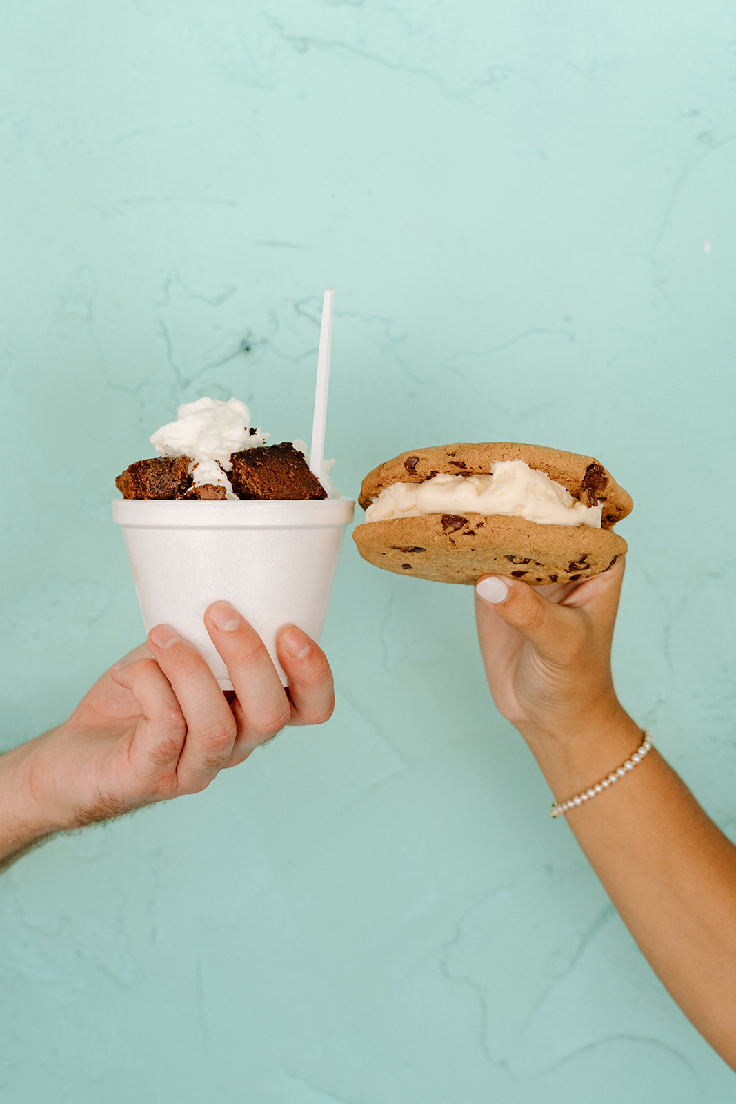 PROCO Hands holding ice cream cookie sandwich and brownie sundae against aqua background, possibly desserts at Southport Seafood Restaurant.
